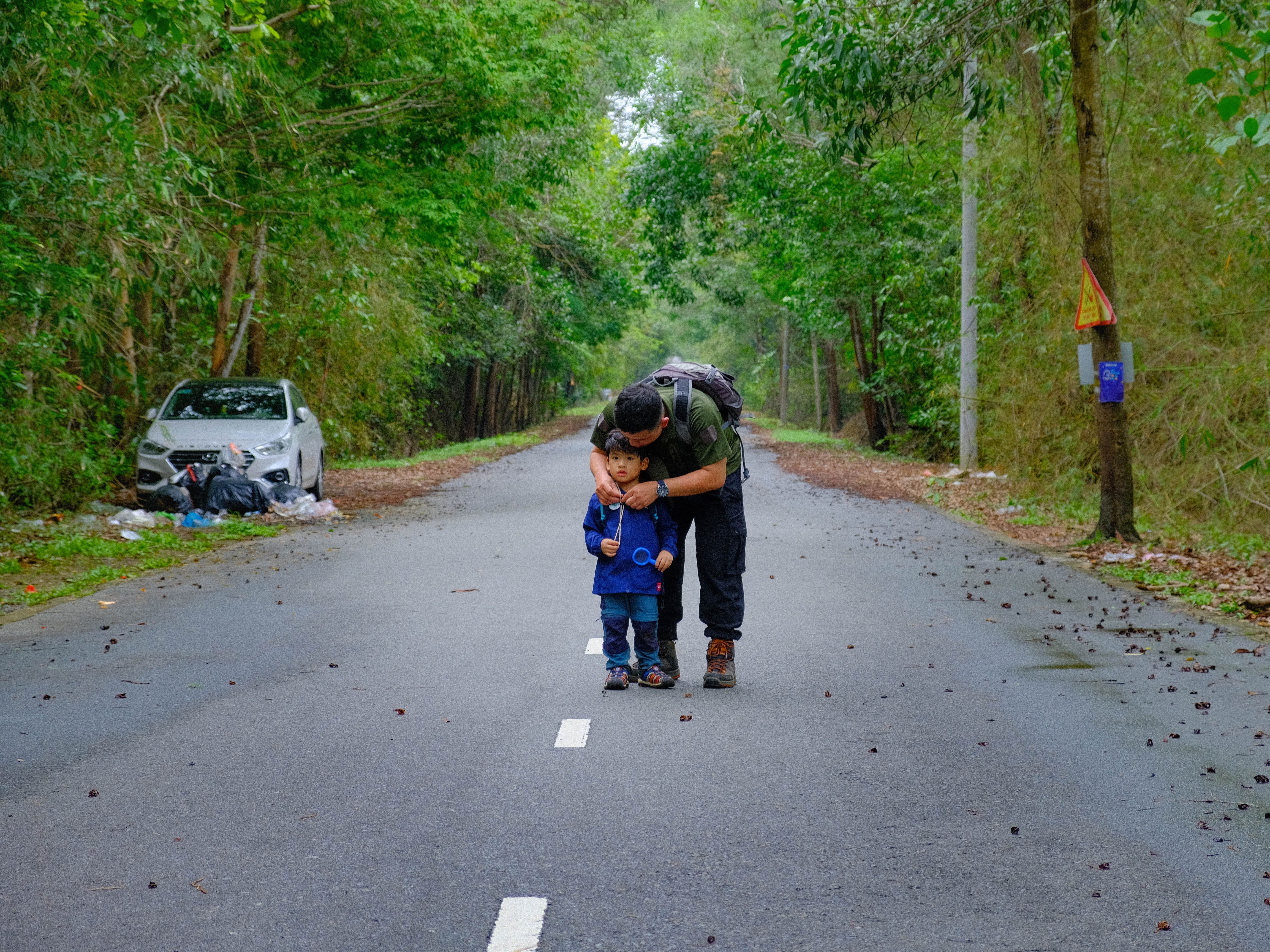 A father and son bonding while walking on a forest road in Ba Ria, Vietnam, surrounded by lush greenery.