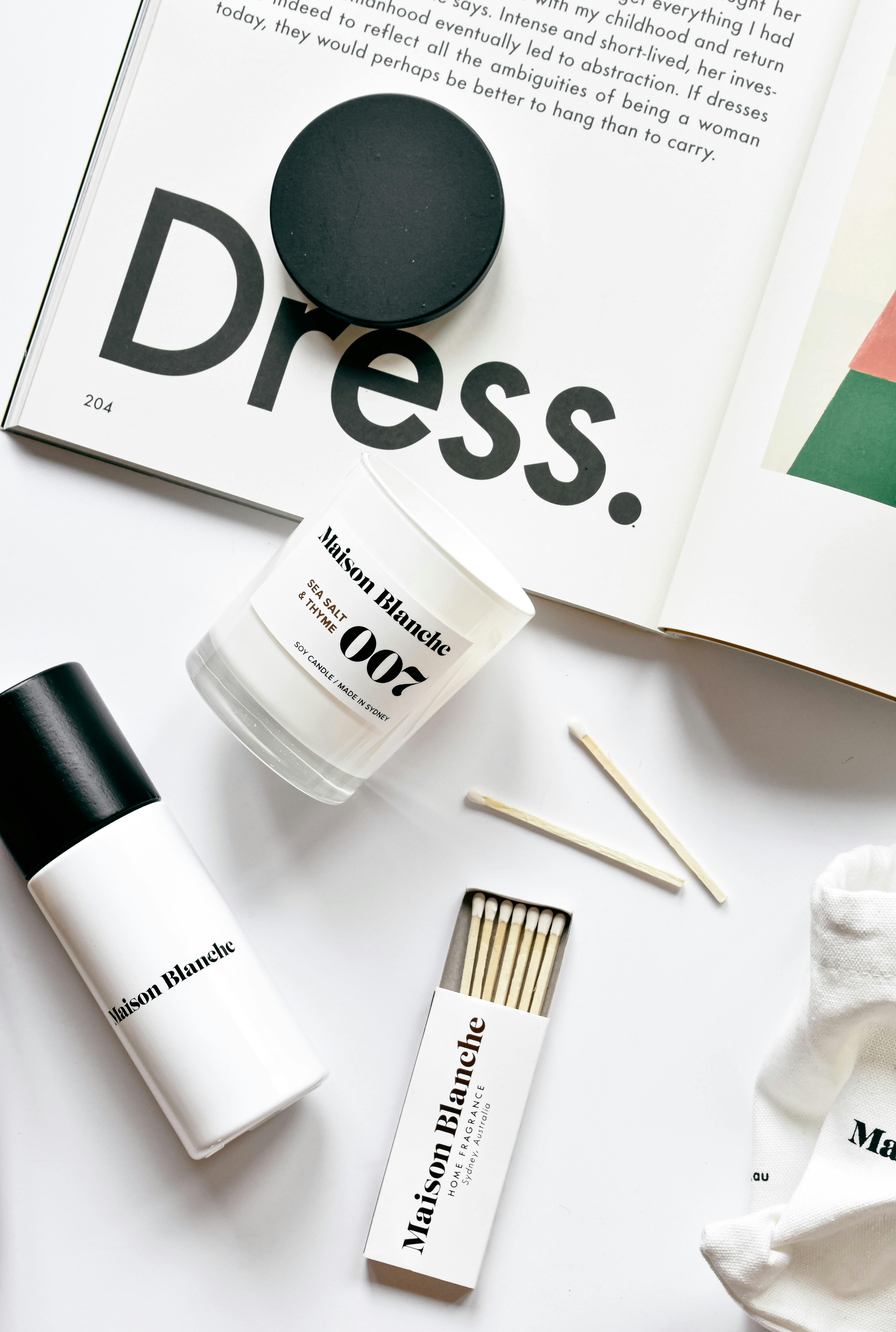 Stylish flat lay with magazine, candle, and cosmetics on a clean white background.
