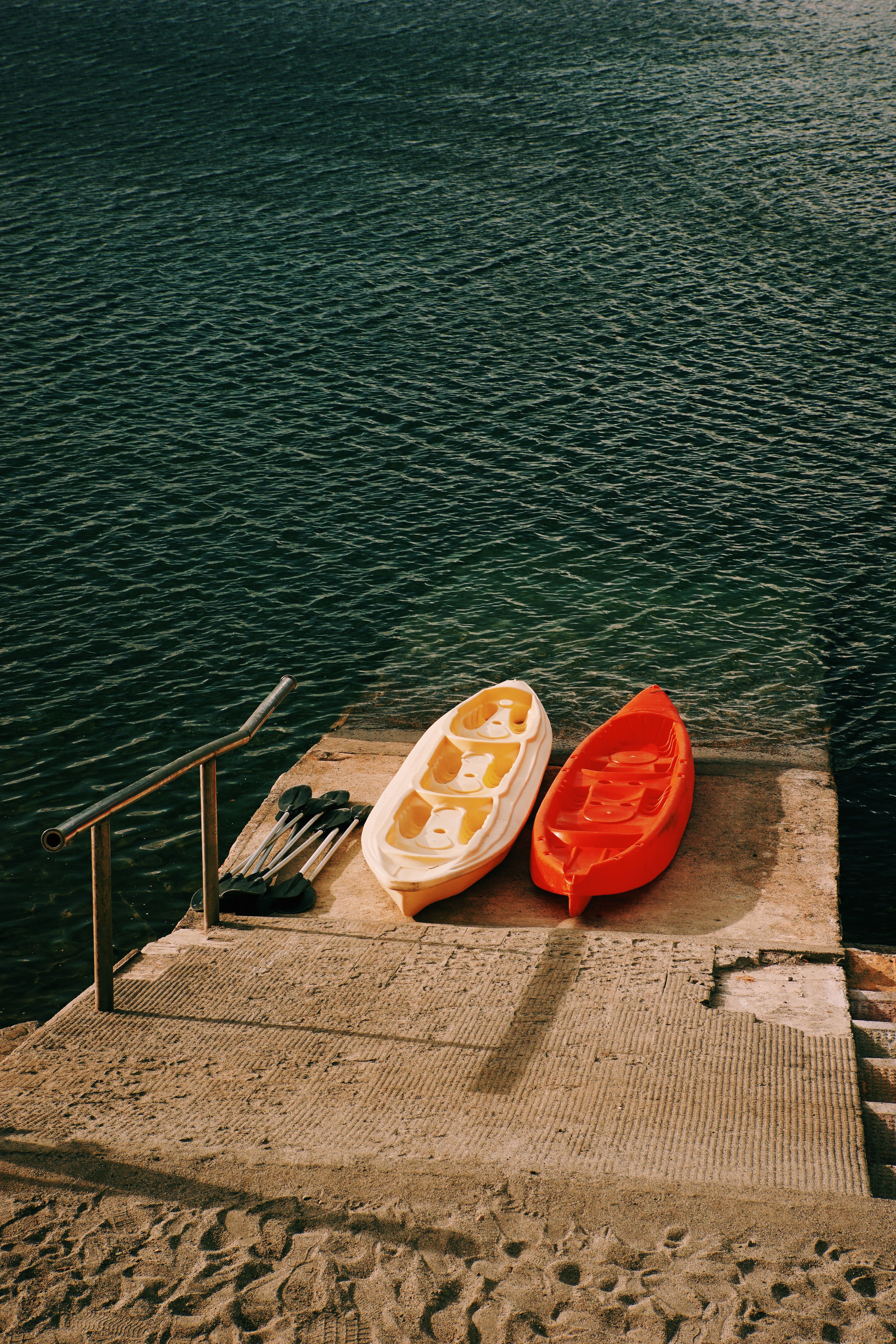 Two kayaks and paddles positioned on a lakeshore slipway beside the water and ready for recreation
