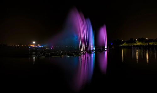 Free Colorful lights illuminate a water fountain at night, reflecting vividly on the river. Stock Photo