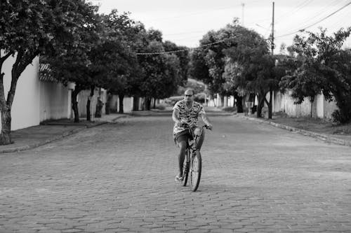 Black and White Photo of a Man in Eyeglasses Riding a Bicycle on an Empty Street