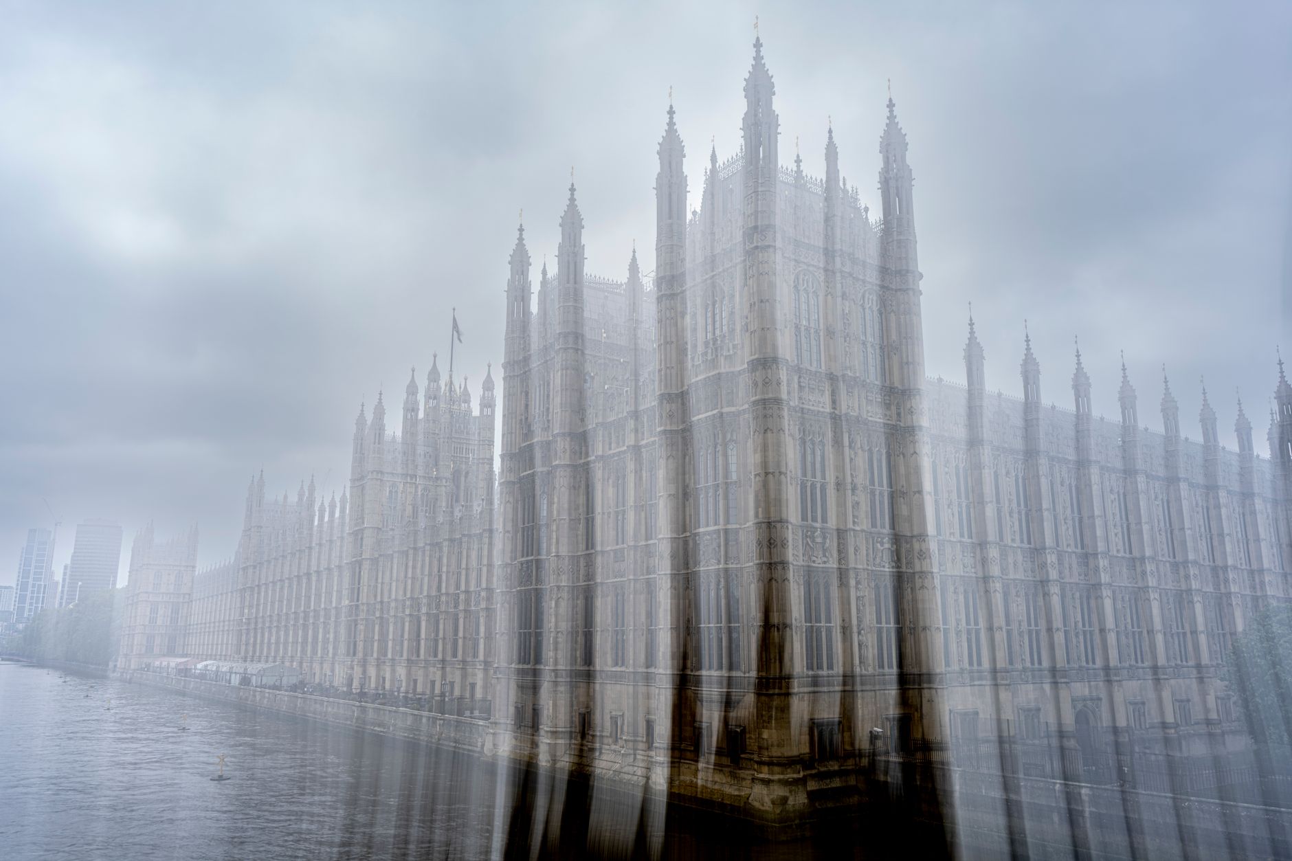 A misty day reveals the iconic architecture of the Palace of Westminster by the Thames.