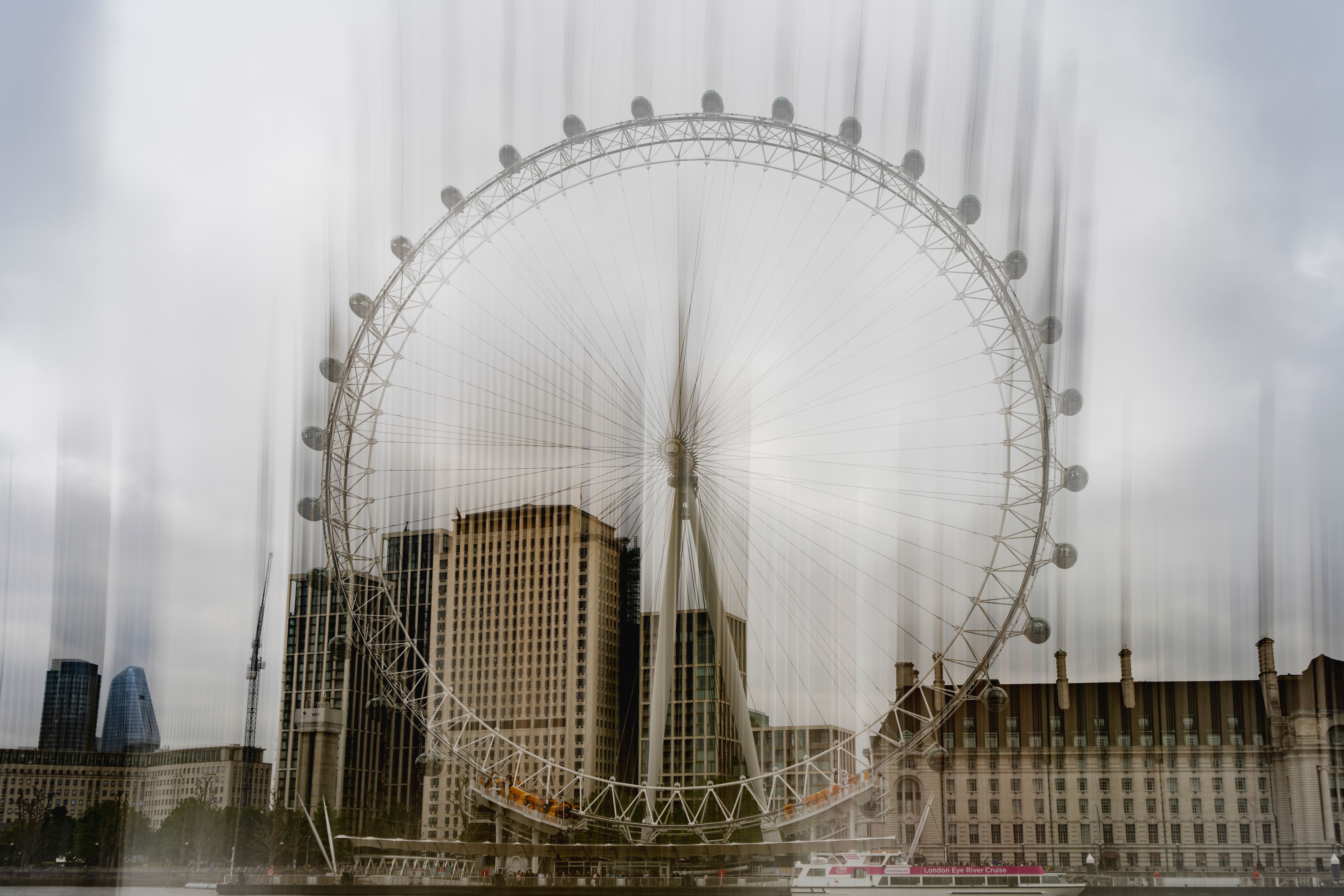 Artistic blurred view of the London Eye against a cloudy London cityscape, creating a dynamic effect.