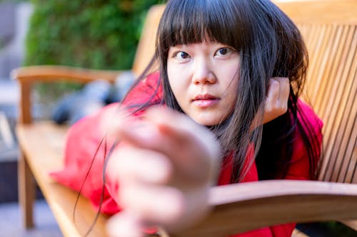 Young Asian Woman Lying Prone on Bench Reaching Towards Camera