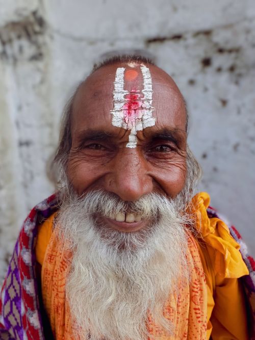 Free Portrait of an elderly man with a joyful smile and religious symbols on his forehead, wrapped in vibrant clothing Stock Photo