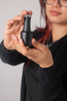 Close-up of a woman with red hair holding a nail polish bottle with care.