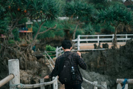 Man walking on a footbridge in a lush rural setting, carrying a backpack. Scenic and serene.