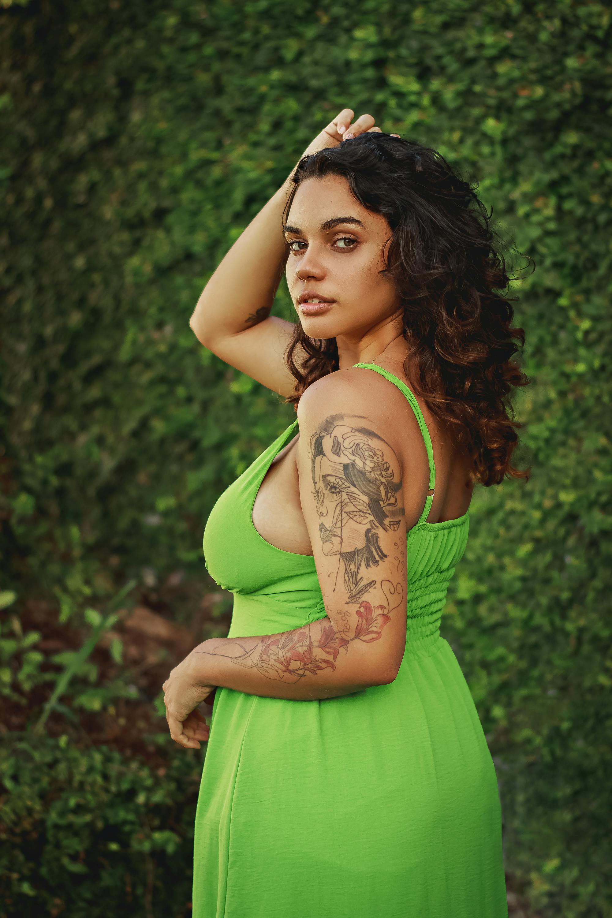 Portrait of a young woman in a vibrant green dress with tattoos, posing confidently outdoors.