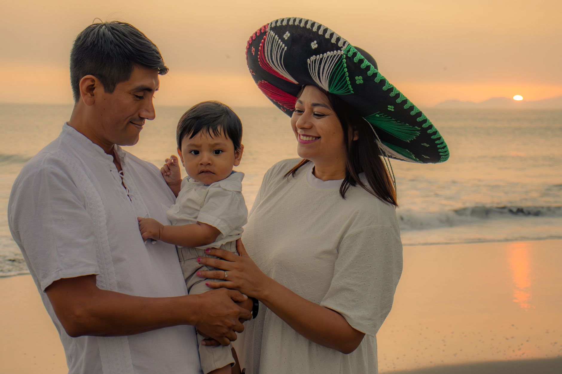 A joyful family enjoys a beach sunset, wearing traditional Mexican attire, capturing warmth and love.