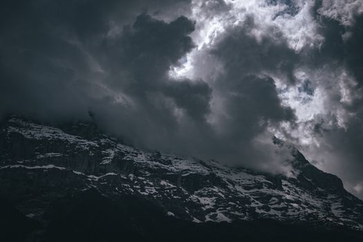 A dramatic view of snowcapped mountains shrouded in dark clouds, creating a moody atmosphere.