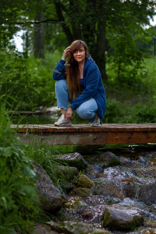 Young Woman Crouching on a Wooden Footbridge over a Stream 