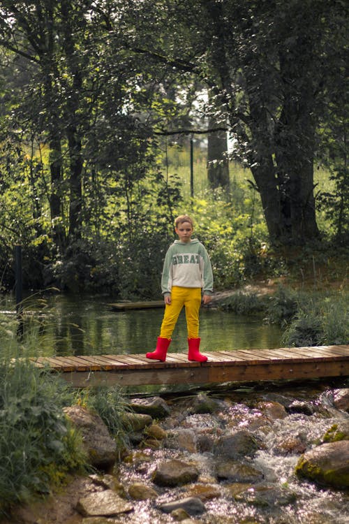 A Boy in Red Rubber Boots Standing on a Footbridge 