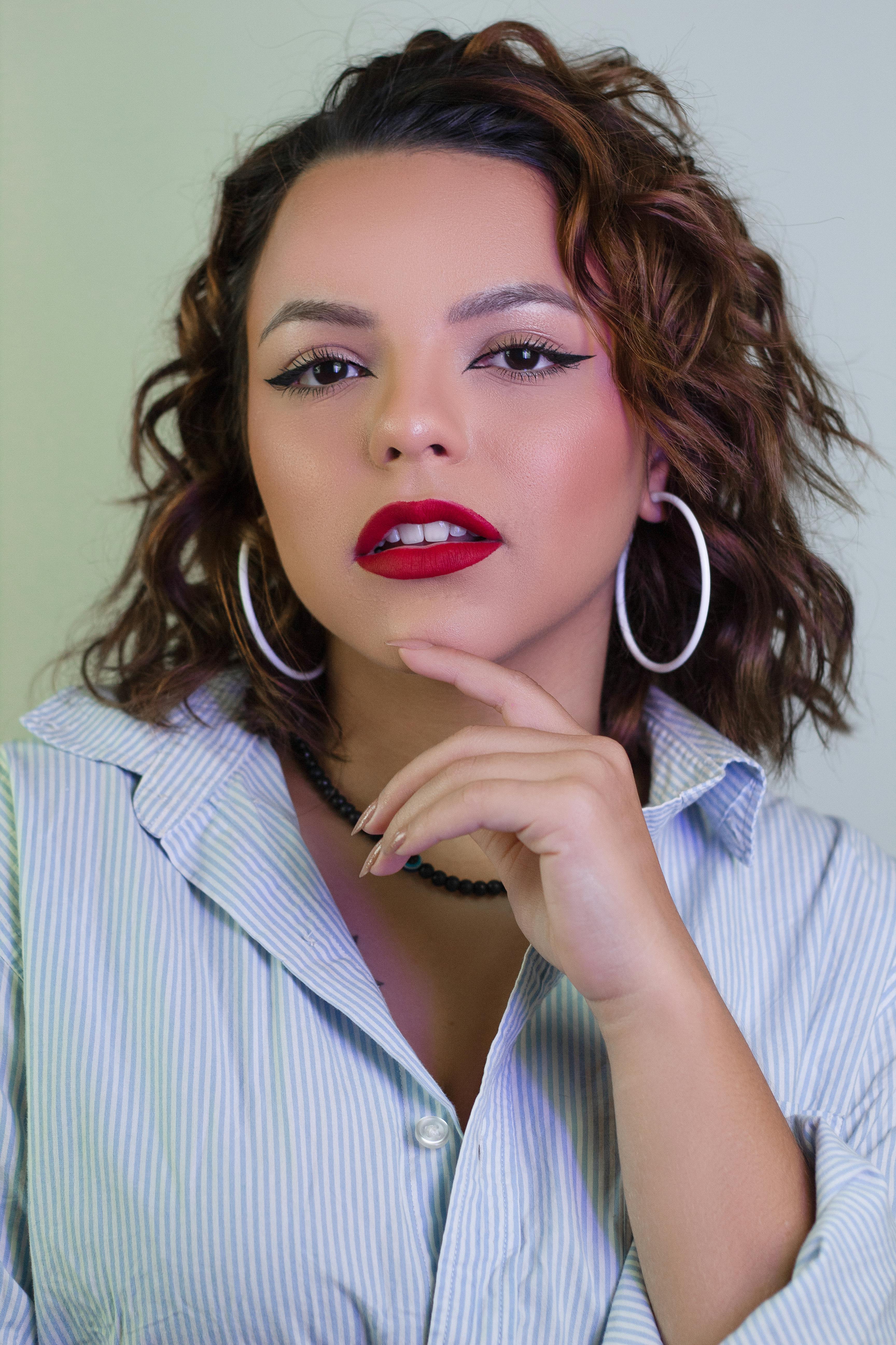 A striking portrait of a woman with bold makeup and hoop earrings, exuding confidence.