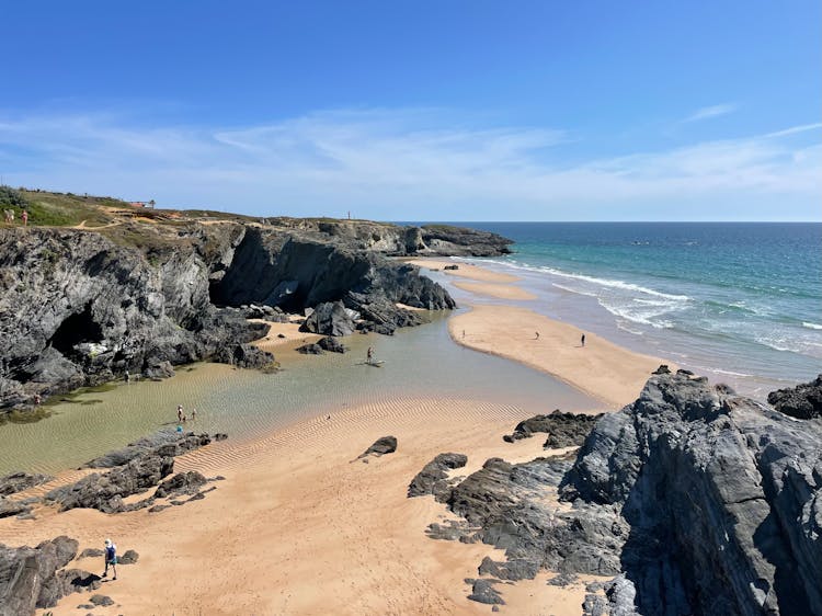 People Walking On Sand Beach With Rocks