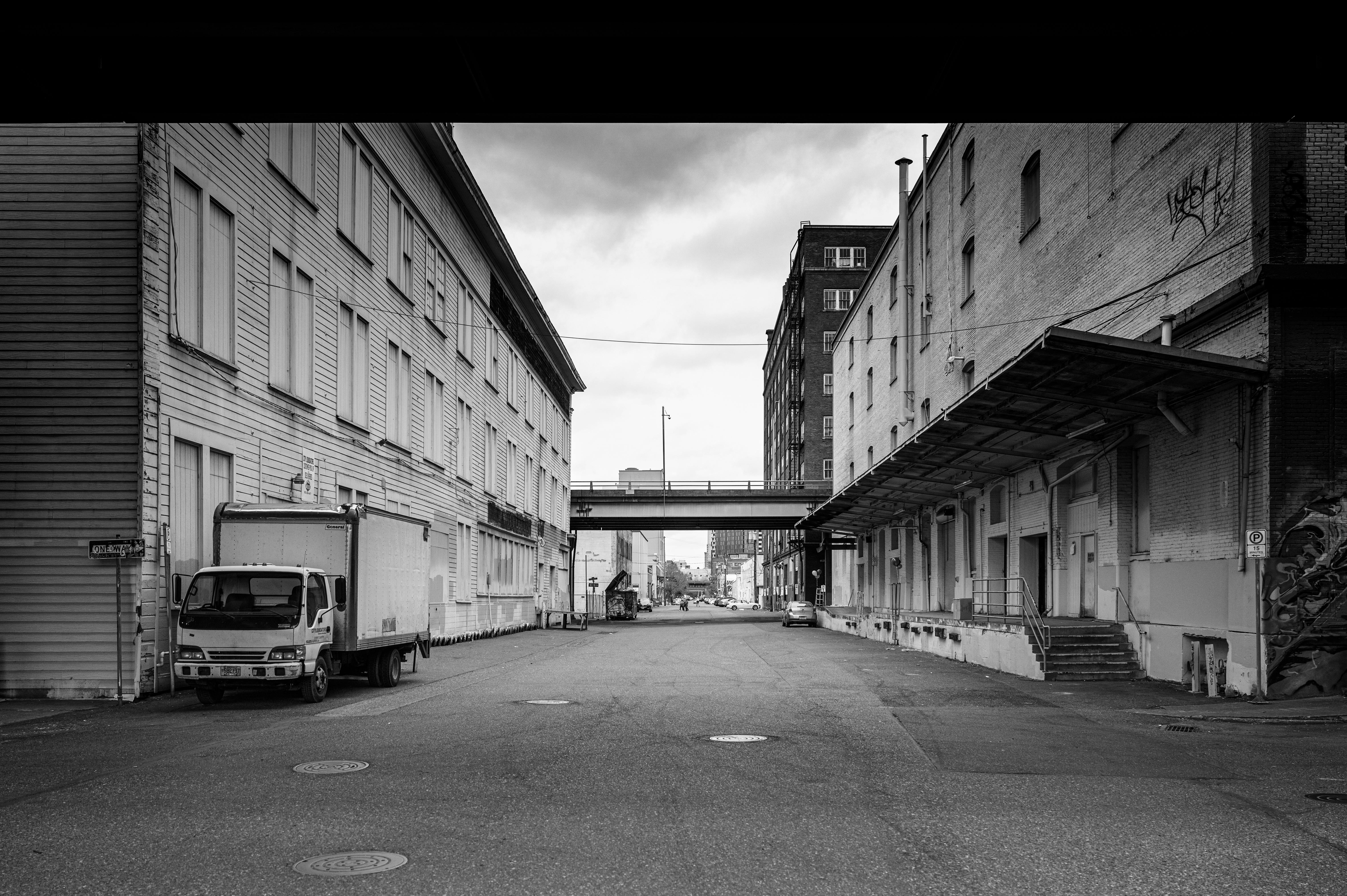 Desolate city street between warehouses in black and white, capturing urban solitude.