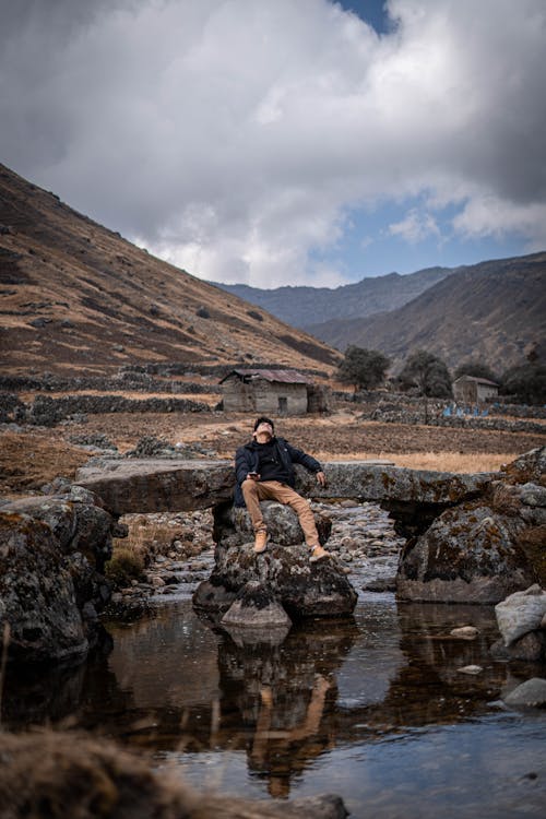 Man Sitting on Stones Supporting a Crumbling Footbridge