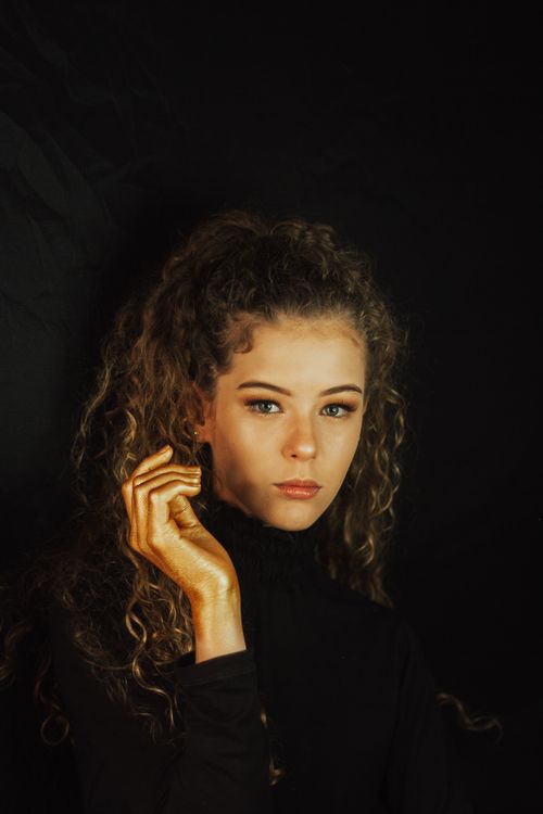 Free Studio portrait of a woman with curly hair and golden hand against a dark backdrop. Stock Photo