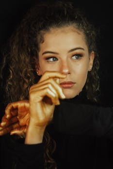 Captivating portrait of a young woman with curly hair and golden painted hands in a thoughtful pose.