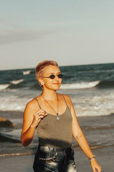 Young fashionable woman with sunglasses walking on the beach, embodying summer vibes and style.