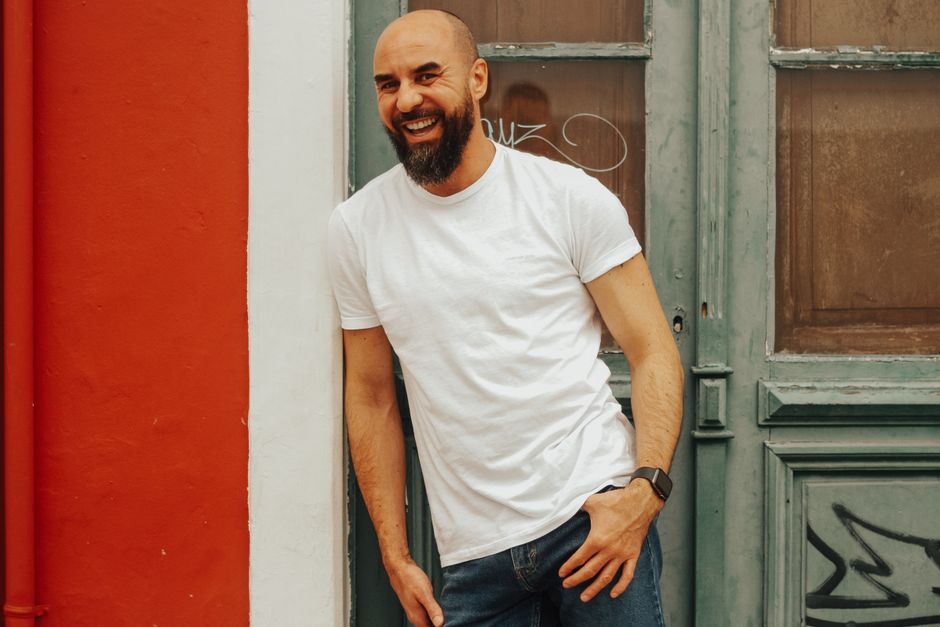 Bald man with a beard smiling and posing in front of a colorful door in Curitiba, Brazil.