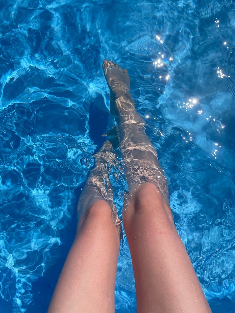 Woman Dipping Feet In A Clear Blue Pool Water