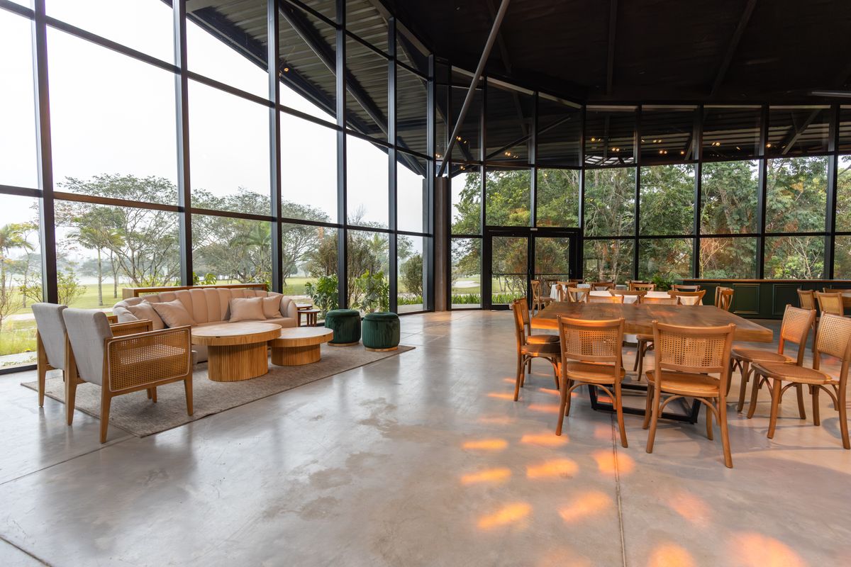 Großer, lichtdurchfluteter Glasraum mit Loungemöbeln und Esstisch, raumhohe Panoramaverglasung zum Garten