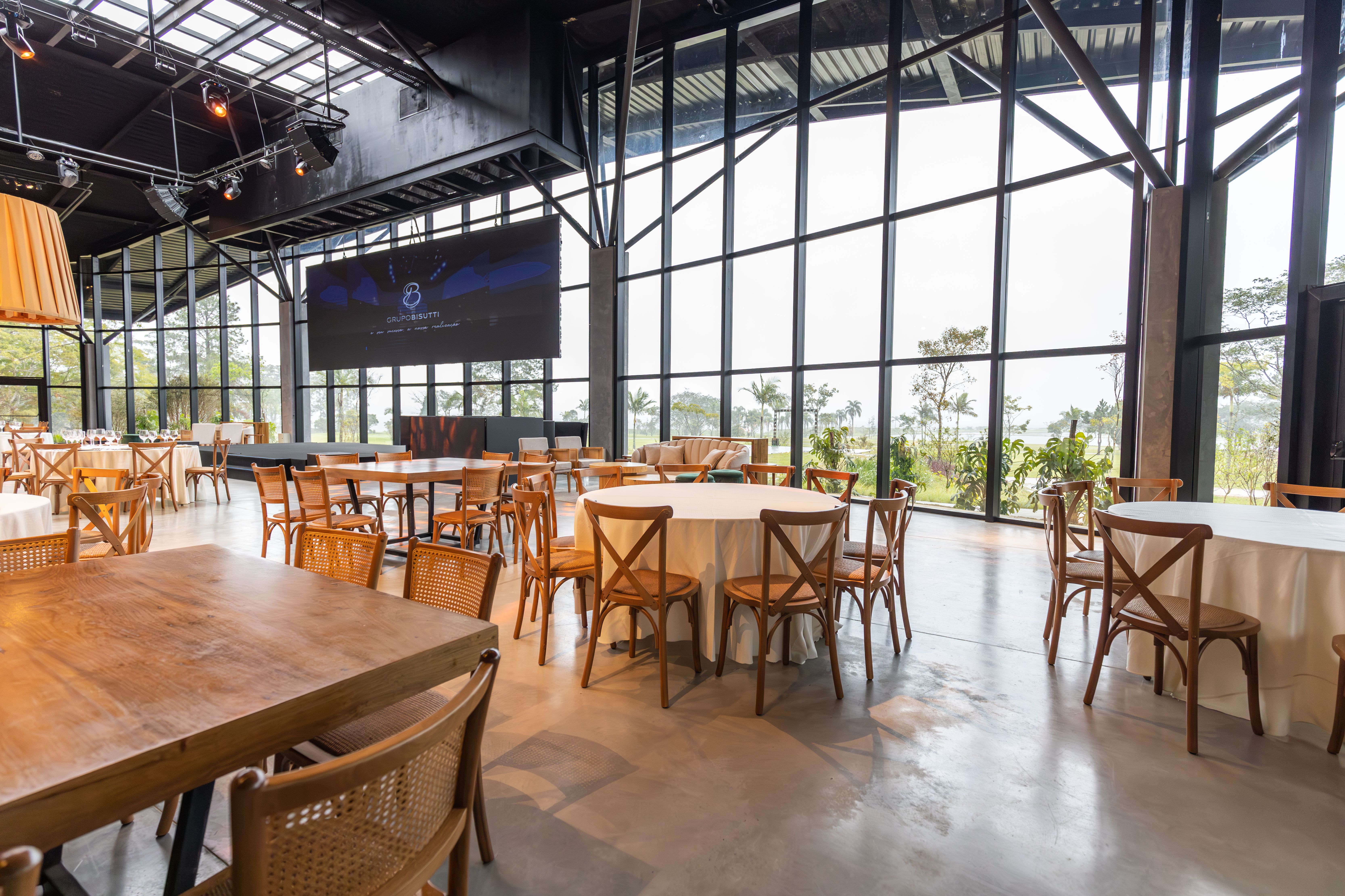 Spacious modern restaurant featuring wooden tables, chairs, and large windows overlooking greenery.