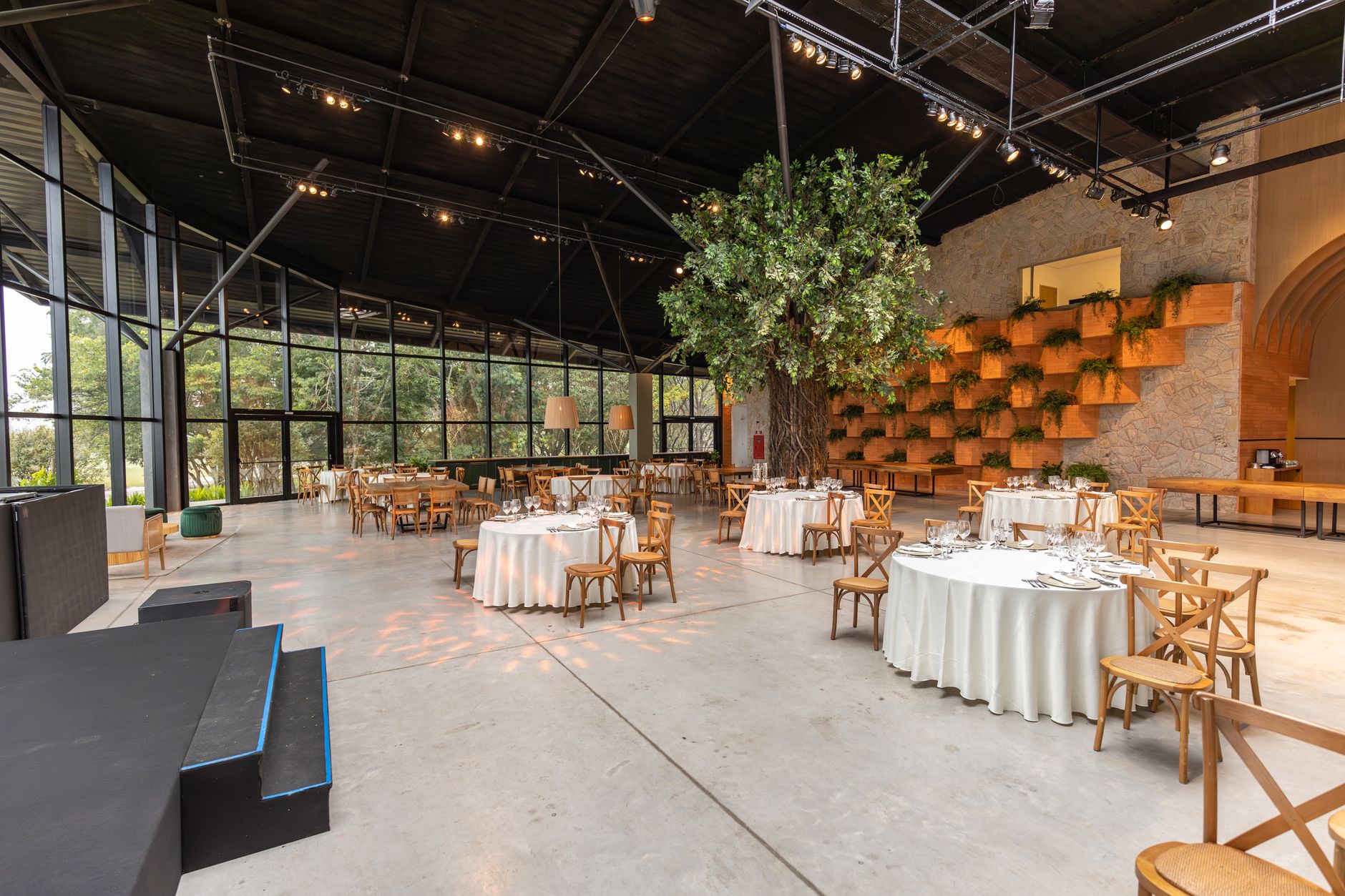 A spacious banquet hall featuring modern decor, lush greenery, and elegant lighting setup for an event.