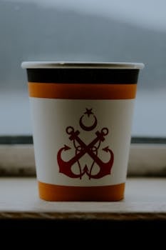 A paper cup with a nautical anchor design in a vertical close-up image.