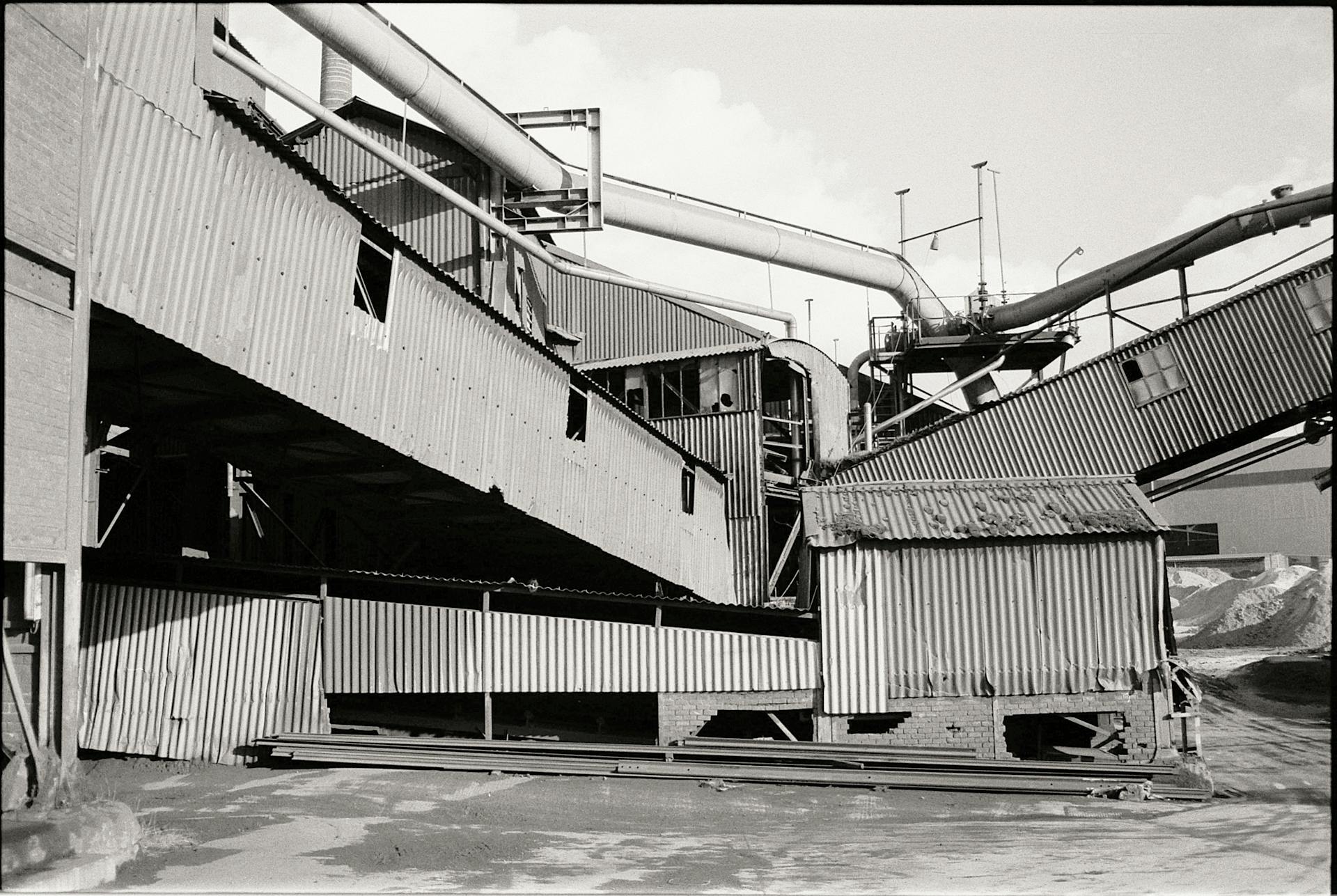 Black and white photo of an abandoned industrial processing plant with pipelines and steel structures.