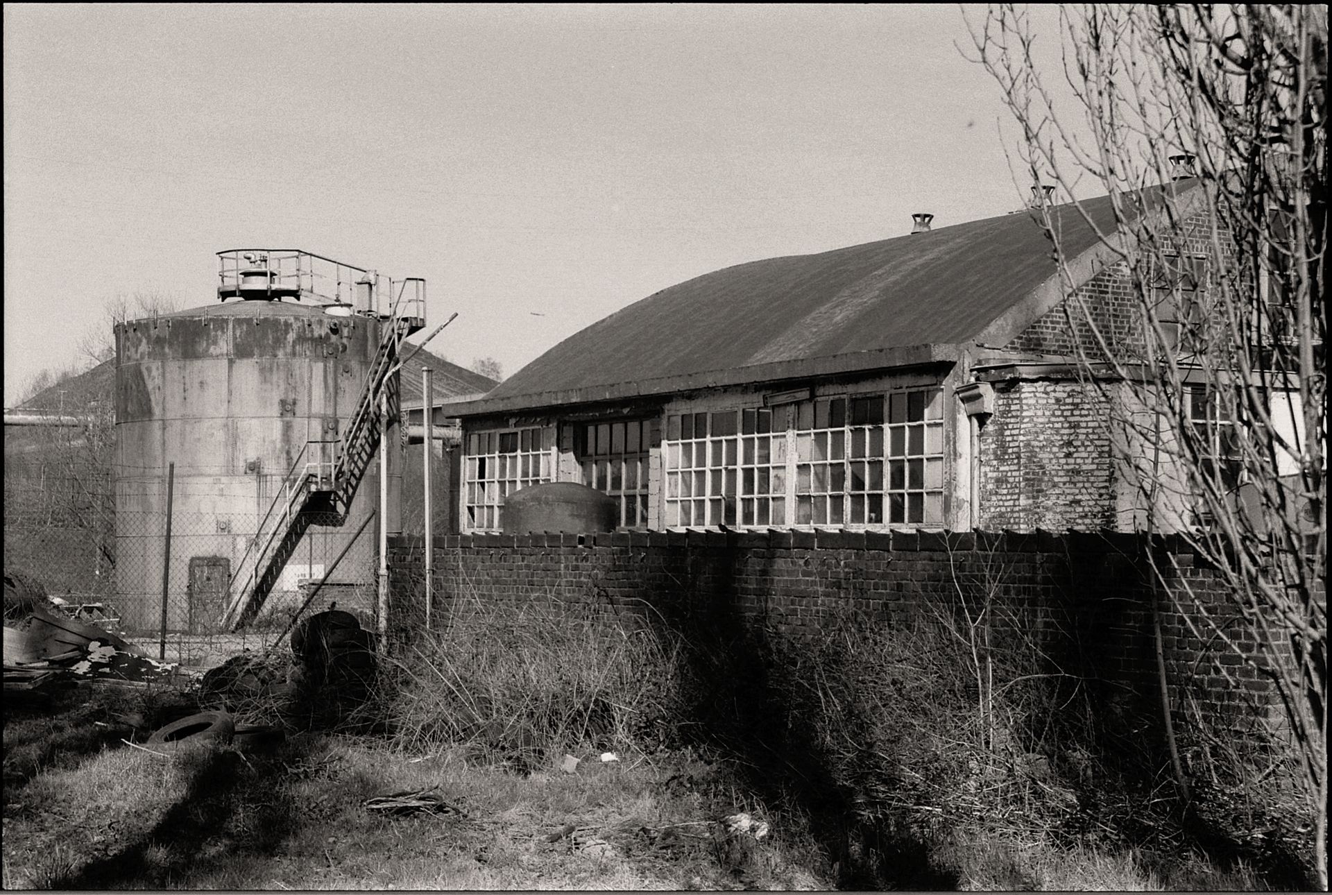 A black and white photograph of an abandoned industrial building and grain bin.
