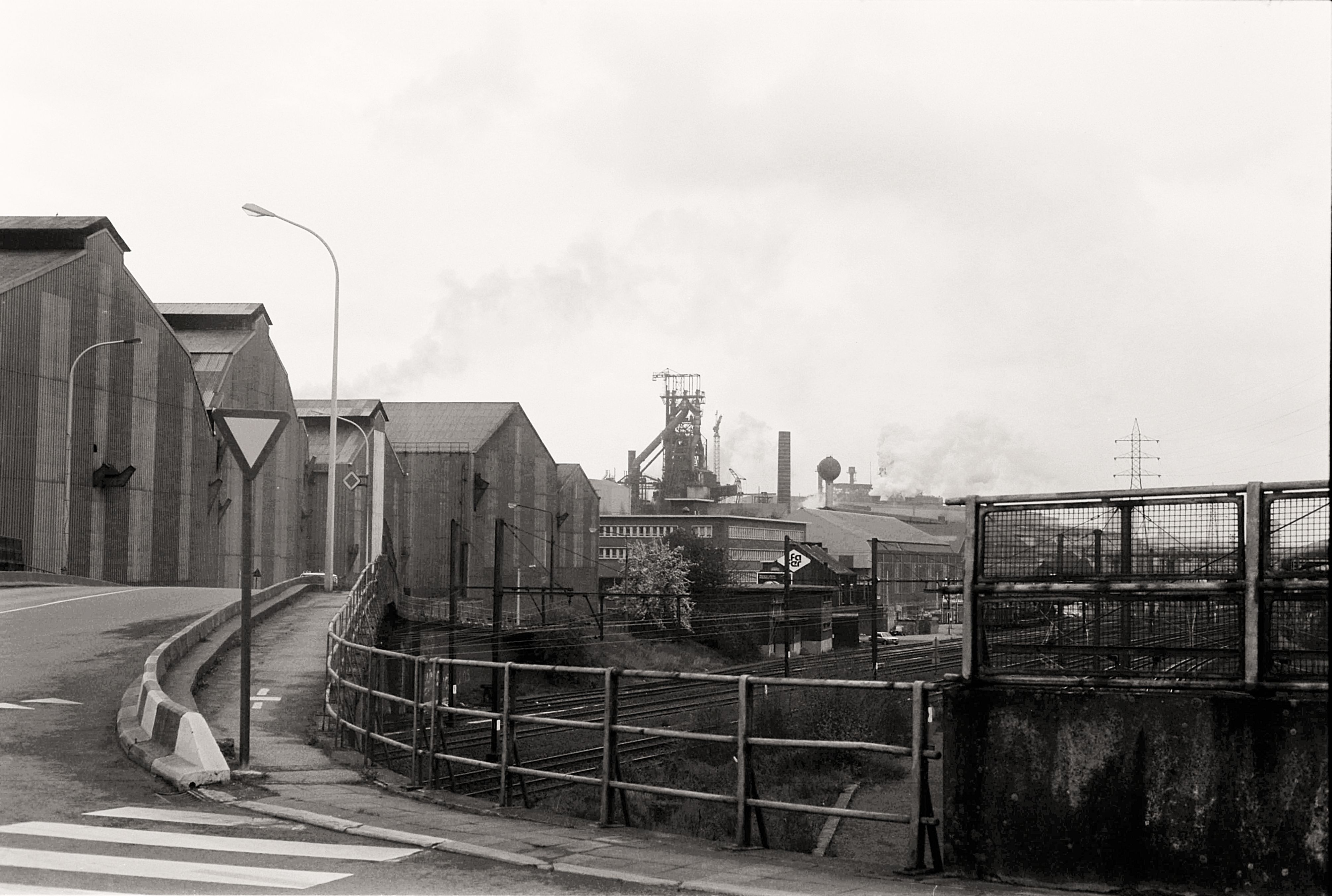 Black and white photo showcasing an industrial section of a city with factories and railways on an overcast day.