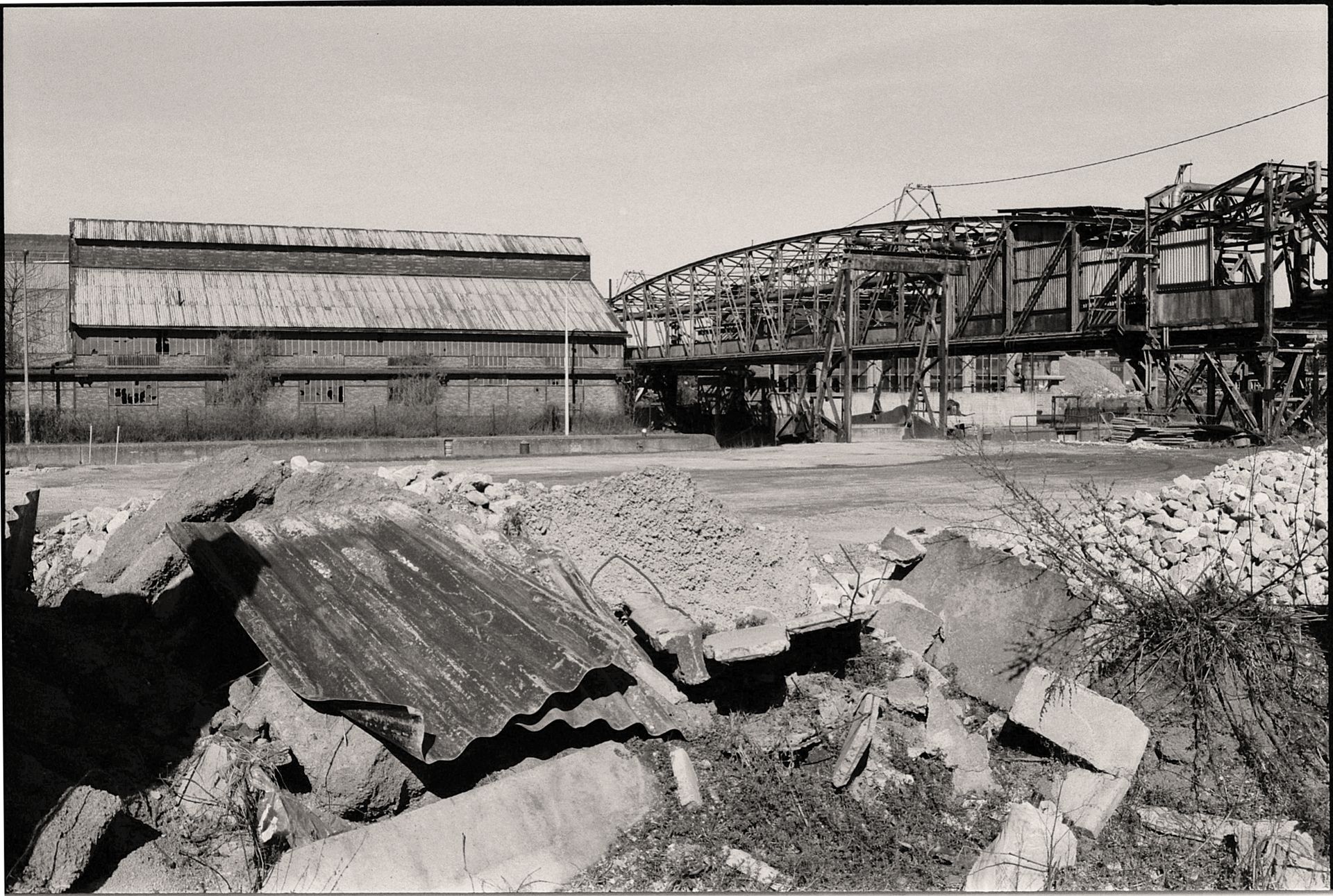 A black and white image of an abandoned factory and bridge, capturing industrial decay.