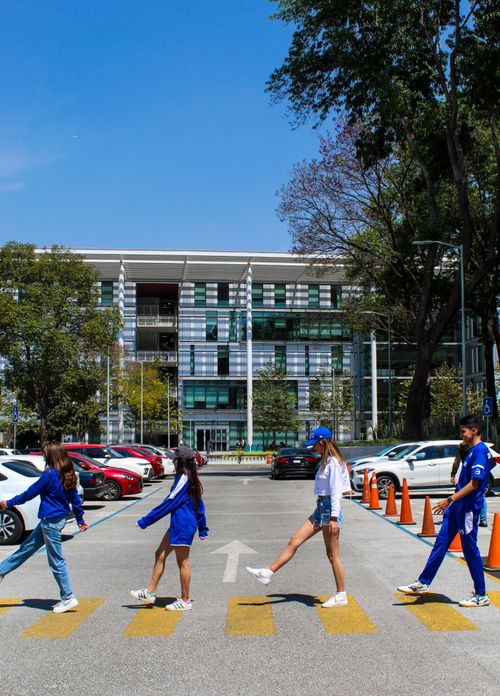 Free A group of university students cross a campus street on a sunny day, engaging in a playful walk. Stock Photo