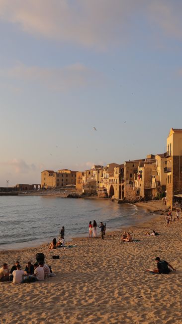 A lively beach scene in a coastal town with historic buildings and people enjoying the warm, sunny day.