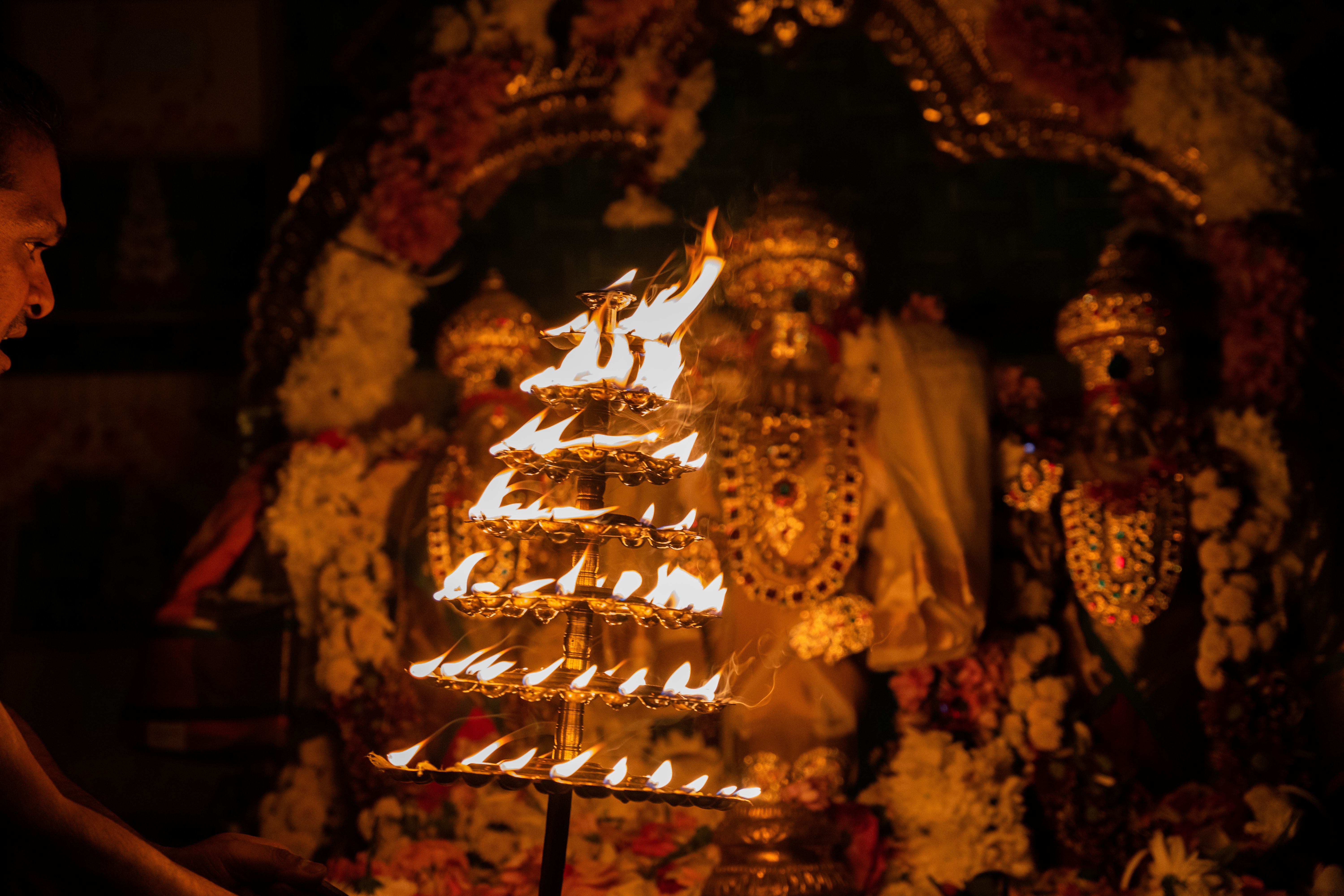 Traditional Hindu ritual with fire offering in front of deity adorned with flowers and jewelry.