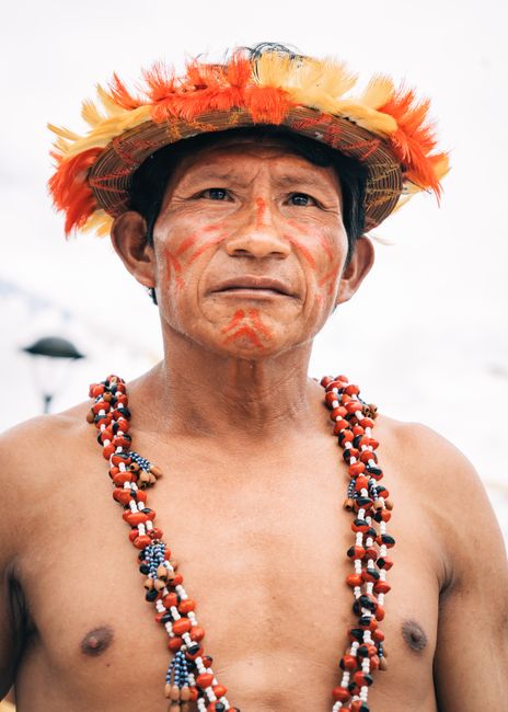 Portrait of an indigenous man in ceremonial dress with feathered hat and beaded necklace, outdoors in Peru.