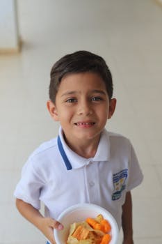 Boy holding a bowl of chips and cheese curls indoors, looking upward.