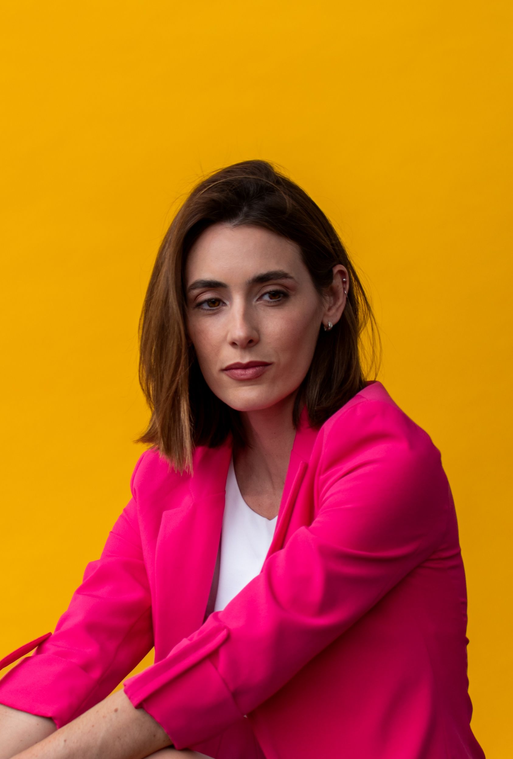 Stylish portrait of a brunette woman in a pink blazer set against a vibrant yellow backdrop.