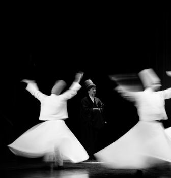 Black and white image of whirling dervishes performing a traditional Sufi dance with motion blur effect.