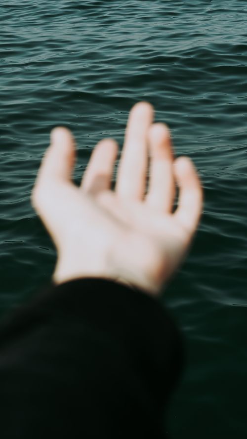 Free Blurred hand extending over the ocean water, creating a serene marine atmosphere. Stock Photo