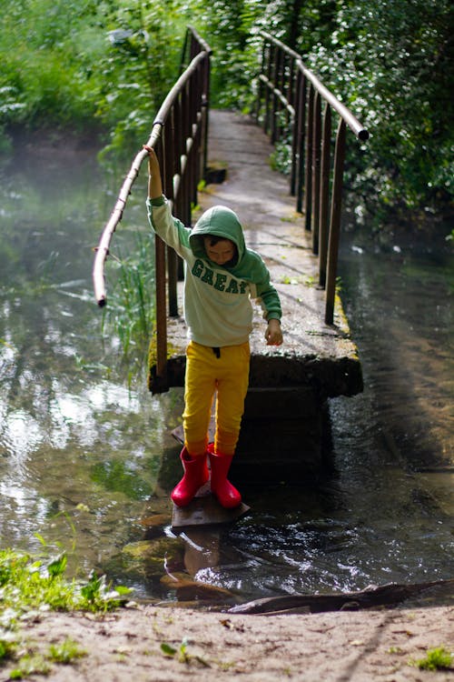 Boy in Hoodie Standing near Water and Footbridge