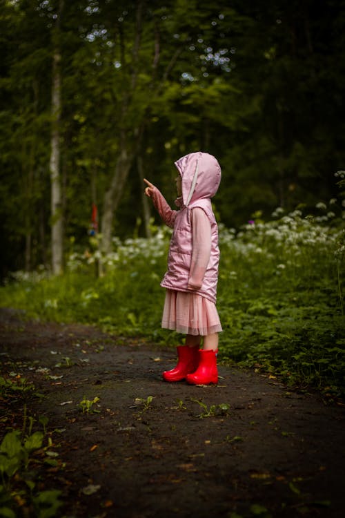 A Little Girl in Rubber Boots and a Pink Jacket Standing in a Park 