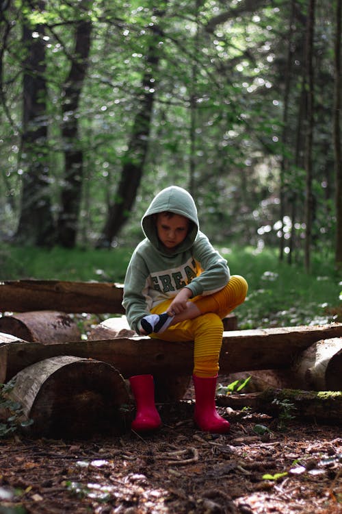 Little Boy Sitting on Wooden Bench in a Forest 