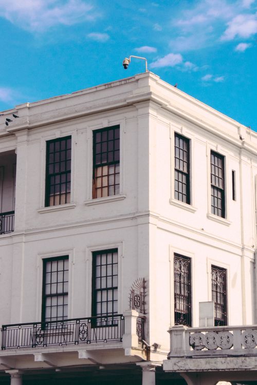 Free A charming urban building featuring classic white walls with black window trims against a clear blue sky. Stock Photo