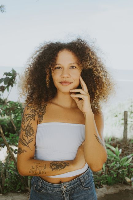 Smiling young woman with curly hair and tattoos posing outdoors in the summer.