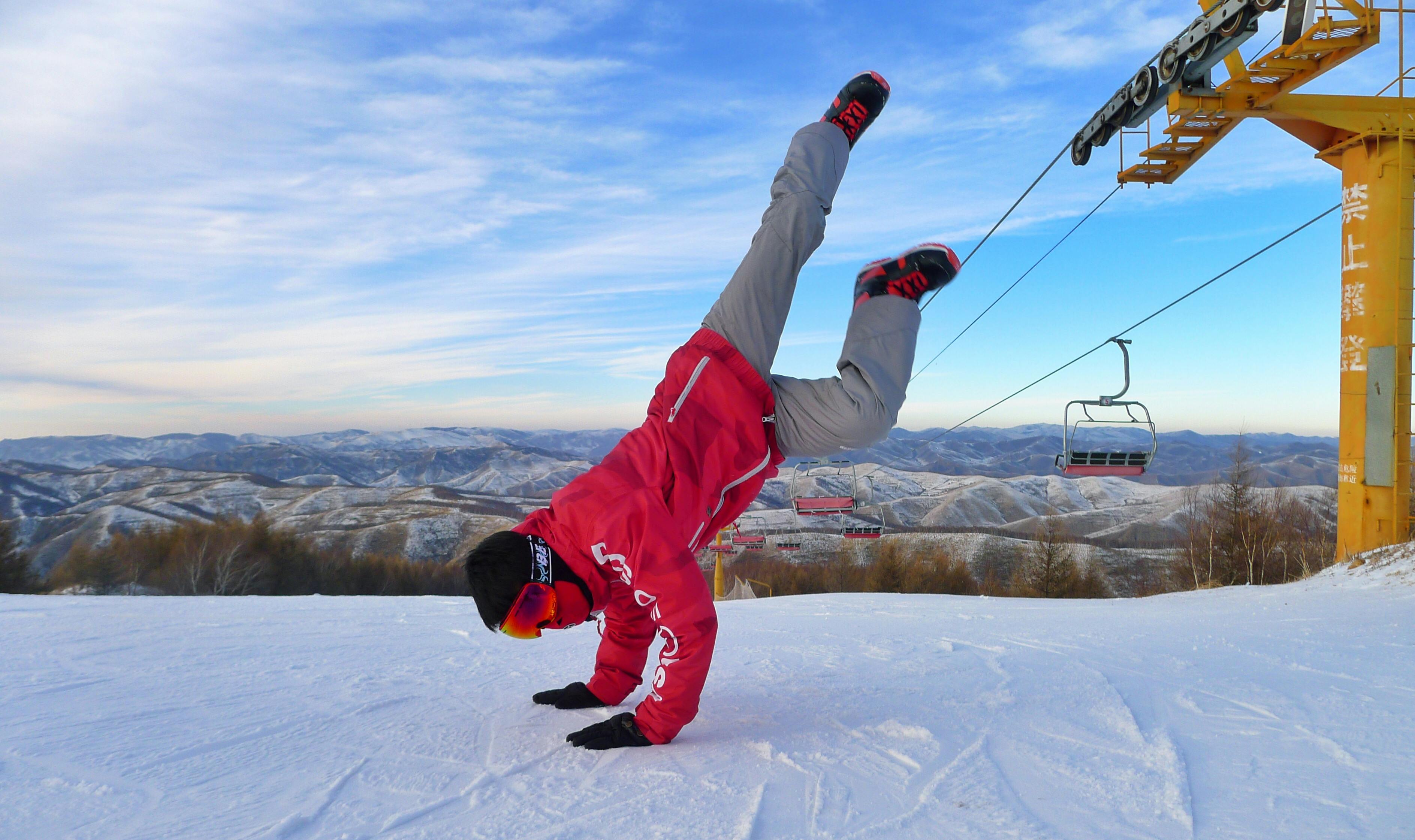 Prescription Goggle Inserts - A man in a red jacket doing a handstand on a snowy mountain with scenic views.