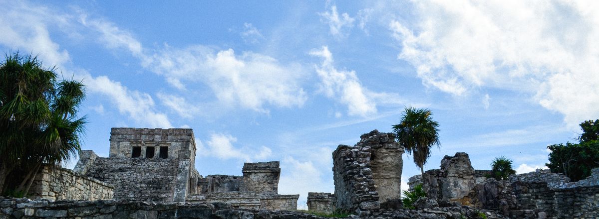 Explore the ancient Mayan ruins of Tulum, featuring historic stone structures against a vibrant sky.