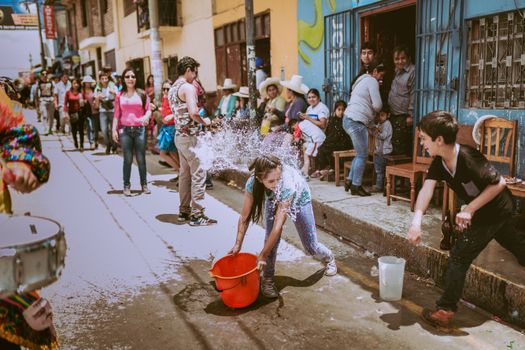 Colorful street festival in Cajamarca, Peru, featuring playful water splashing among children and locals.