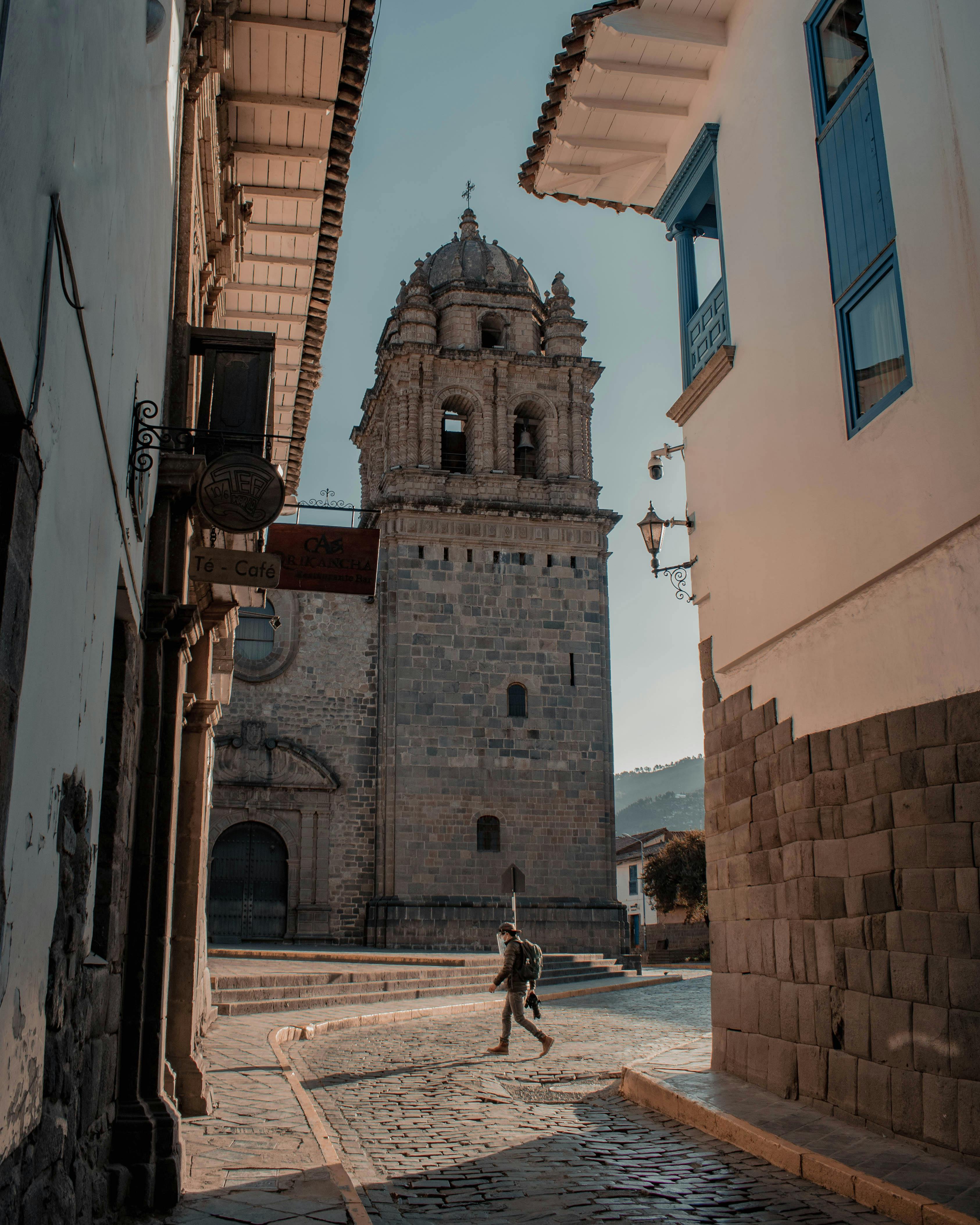 Photograph of a historic tower and cobblestone street in Cusco, Peru, highlighting colonial architecture.